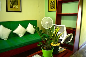 A green sofa with white cushions, a white chair, a green potted plant, and a white fan on a wooden table. - CHOLSON CHALETS LIMITED (Charlotteville)