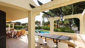 Eine Außenpatio mit Tisch und Stühlen, ein Pool im Hintergrund und Blick auf die grüne Umgebung.