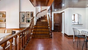 Eine Treppe mit Holzbalkonen führt zu einer Zwischenebene, einem Essbereich mit Tisch und Stühlen sowie einer Küche mit Fenster und Arbeitsfläche.