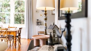 Una habitación acogedora con una mesa de comedor de madera, sillas, una lámpara y una pequeña maqueta de una casa.