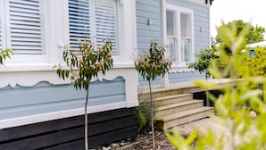 Una casa con porche, escalones que llevan a la entrada y un árbol pequeño al frente.