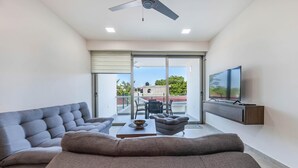 A modern living room with a grey sofa, a coffee table, and a TV mounted on the wall. - Modern 1 BR Condo w/ Ocean View Infinity Pool (Isla Mujeres)