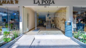 The entrance to La Poza Condominium with a stone wall interior, glass doors, and a blue trash bin. - Modern 1 BR Condo w/ Ocean View Infinity Pool (Isla Mujeres)