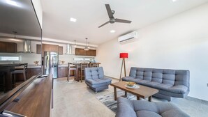 A modern living room with a sofa, a coffee table, and a dining area with a kitchen in the background. - Modern 1 BR Condo w/ Ocean View Infinity Pool (Isla Mujeres)