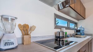 A kitchen with a blender, wooden utensils, a water dispenser, and a window with a view. - Modern 1 BR Condo w/ Ocean View Infinity Pool (Isla Mujeres)