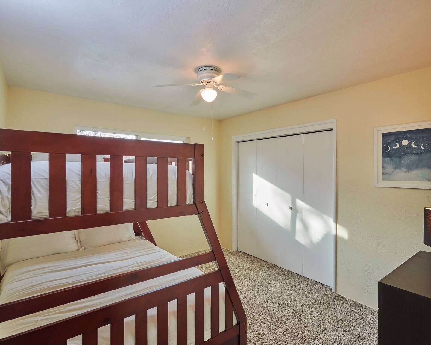 A bedroom with a bunk bed, a ceiling fan, a closet, and a painting on the wall.