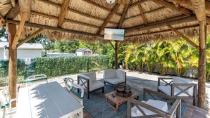 Eine Terrasse im Freien mit Holzmöbeln, einem Deckenventilator und einem Fernsehbildschirm.
