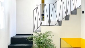 Un escalier avec des marches noires et une rampe aux motifs géométriques, une plante en pot et deux vases décoratifs.