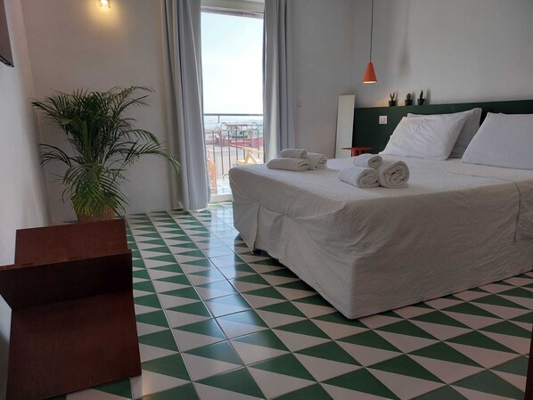 A hotel room with a bed, a potted plant, a green and white checkered floor, and a view of the outside.