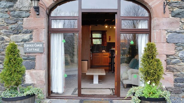 L’entrée du cottage Doddick Chase, avec ses murs en pierre, sa porte en bois et une cuisine visible à l’intérieur.