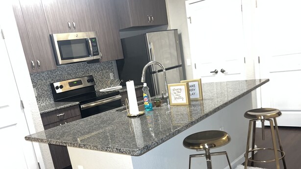 Una cocina moderna con gabinetes de madera oscura, electrodomésticos de acero inoxidable, encimera de granito y alfombra mullida blanca.