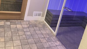 Un vestíbulo de sauna con puerta de vidrio, letrero de baño de vapor y conducto de ventilación.