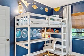 Um quarto com uma cama beliche, uma escrivaninha com cadeira e uma janela com vista.