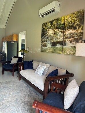 A living room with a sofa, a wooden cabinet, a refrigerator, and a wall-mounted air conditioner.