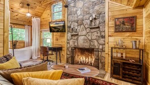 A cozy cabin interior with a stone fireplace, wooden walls, a comfortable seating area, and a desk.