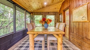 A wooden cabin with a large dining table, chairs, and a vase of flowers.