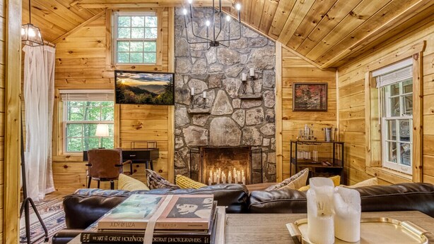 A cozy cabin interior with a stone fireplace, wooden walls, and a comfortable seating area.