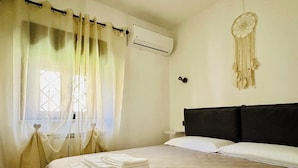 Una cama bien hecha con sábanas blancas, cabecera negra y un atrapasueños en la pared.