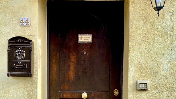 Una puerta de madera con pomo de latón, un buzón, una lámpara de pared y un timbre.