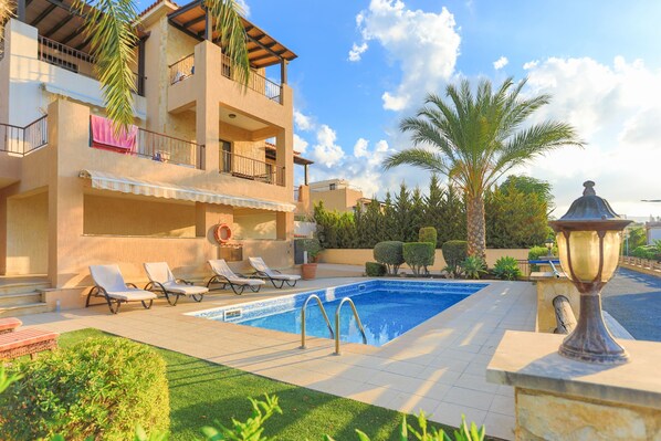A pool area with lounge chairs, a swimming pool, and a building with balconies. - Villa Arbanassi Latchi, beach, pool, A/C, WiFi, garden, views (Latchi Beach)