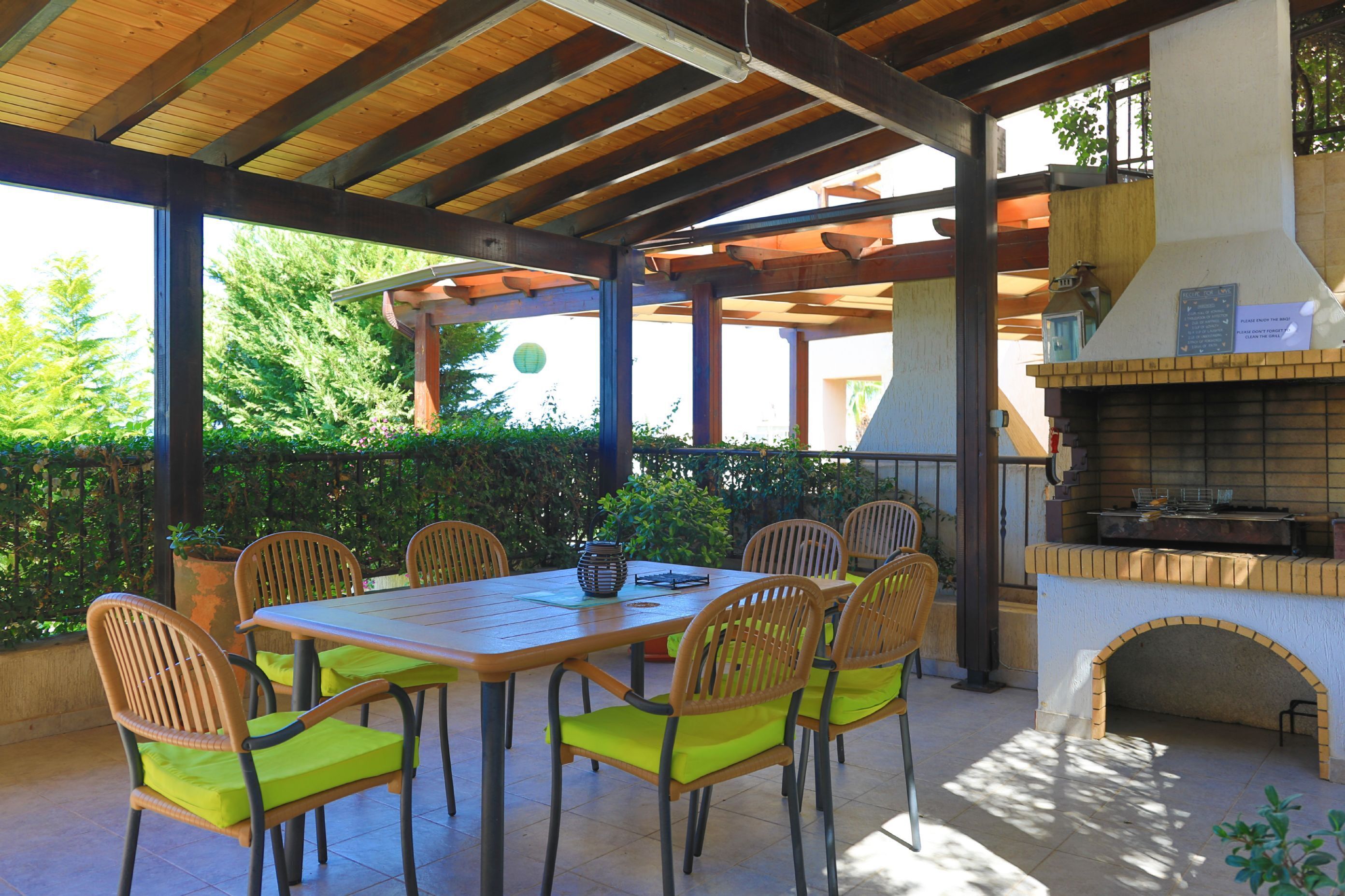 An outdoor patio with a wooden table and chairs, a brick oven, and a pergola structure.