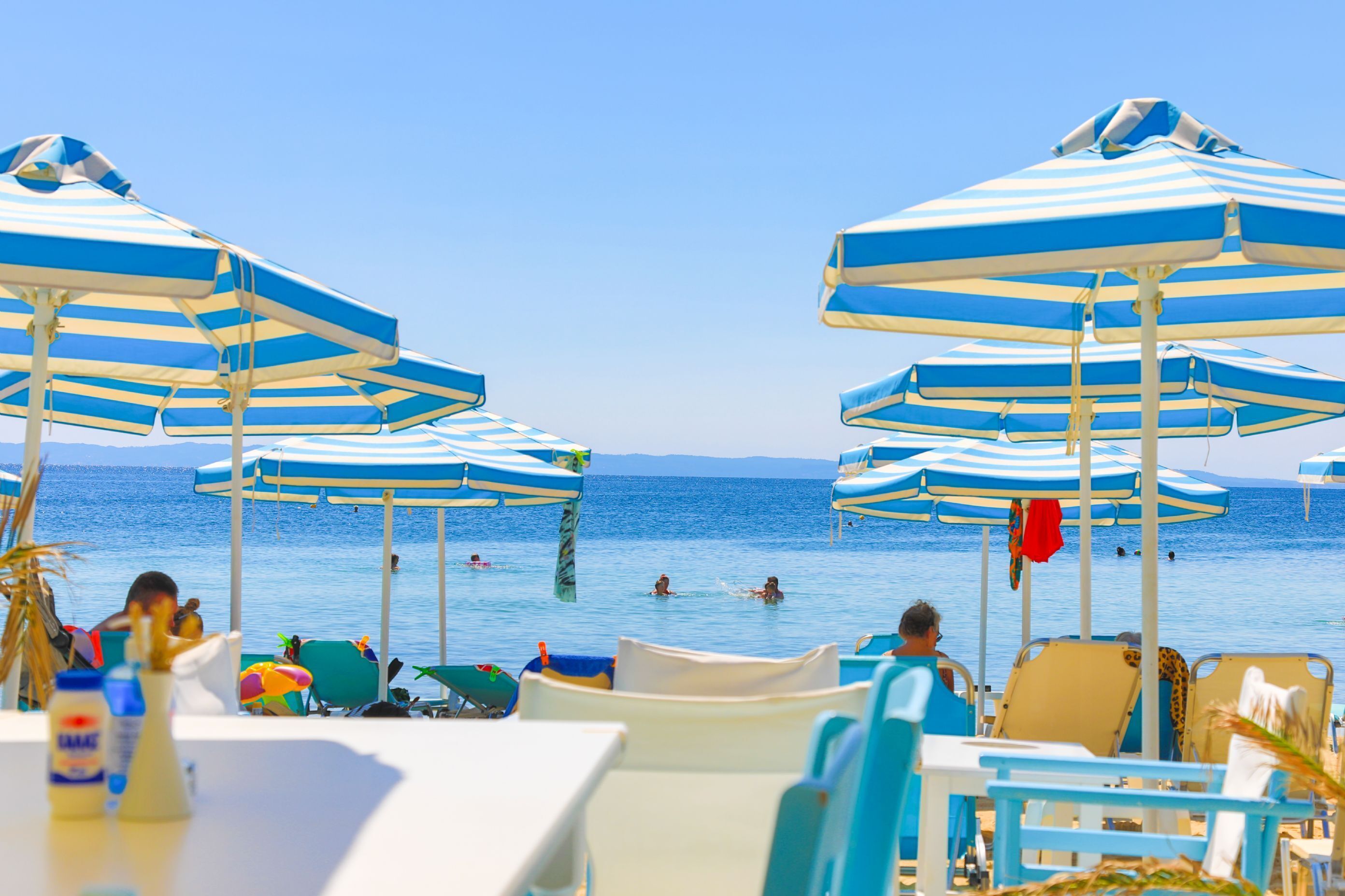 A beachside area with multiple blue and white striped umbrellas, lounge chairs, and tables.
