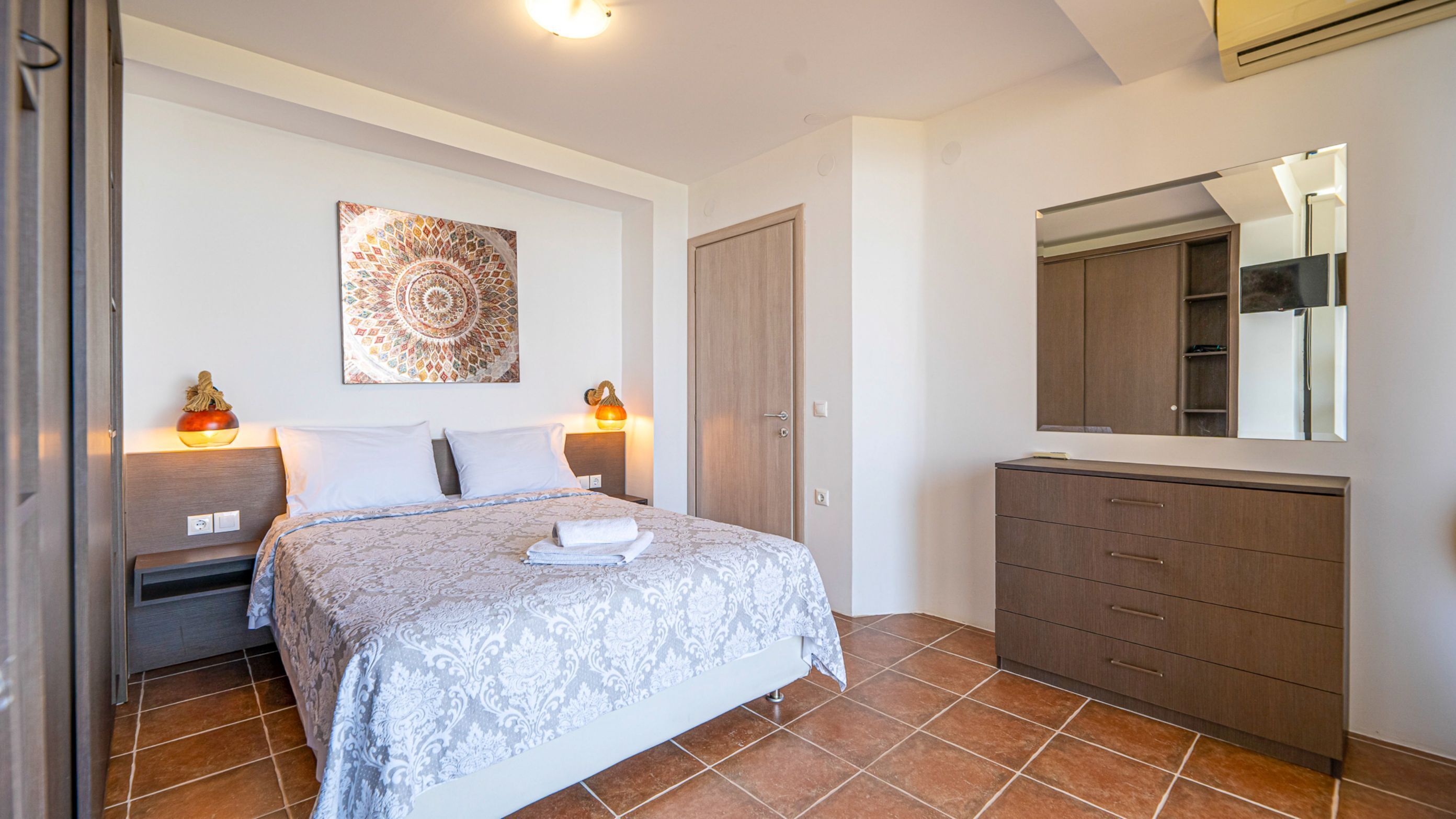 A bedroom with a bed, bedside tables, a wardrobe, a mirror, and a decorative wall piece.