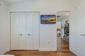 A hallway with a white door, a painting of a sunset, and a bookshelf with books and a radio. - The Laguna Beach: 2 Blocks to Beach, Pool, 5 Hole Put Put, Foosball, Cornhole by Anna Maria Life (Anna Maria)
