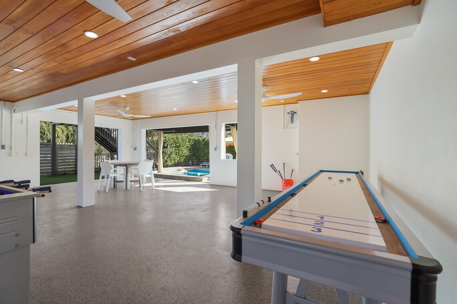 A spacious indoor area with a pool table, a dining table with chairs, and a staircase leading to an outdoor area.