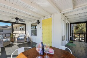 A covered outdoor patio with wicker furniture, a wooden table with wine glasses, and a yellow door. - The Laguna Beach: 2 Blocks to Beach, Pool, 5 Hole Put Put, Foosball, Cornhole by Anna Maria Life (Anna Maria)