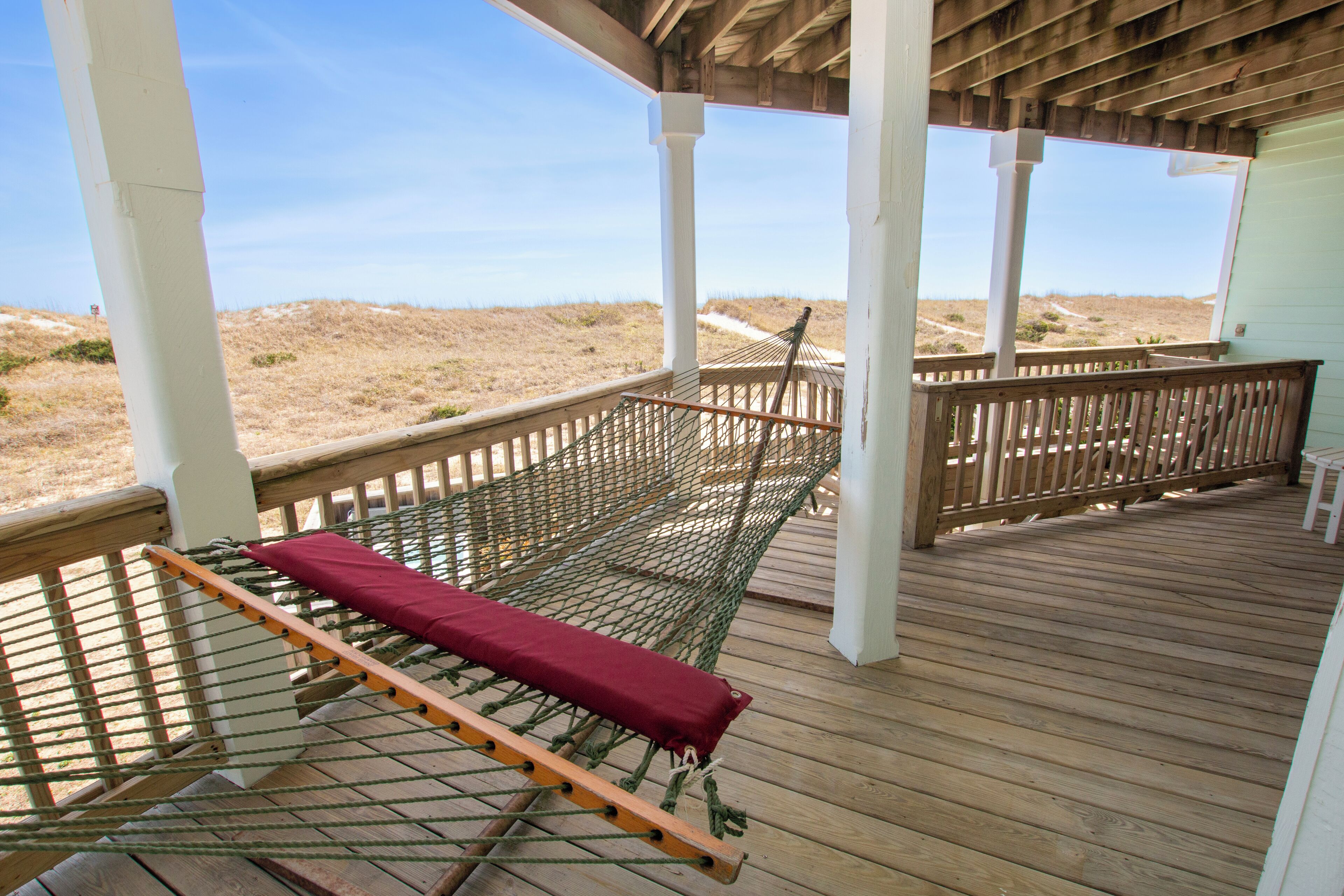 A hammock on a wooden deck with a view of the beach.
