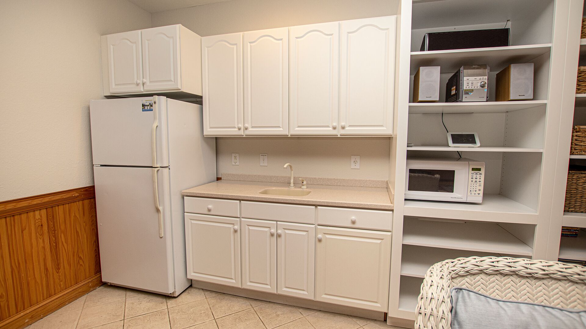 Cocina compacta con armarios blancos, un refrigerador, un microondas y un lavamanos.