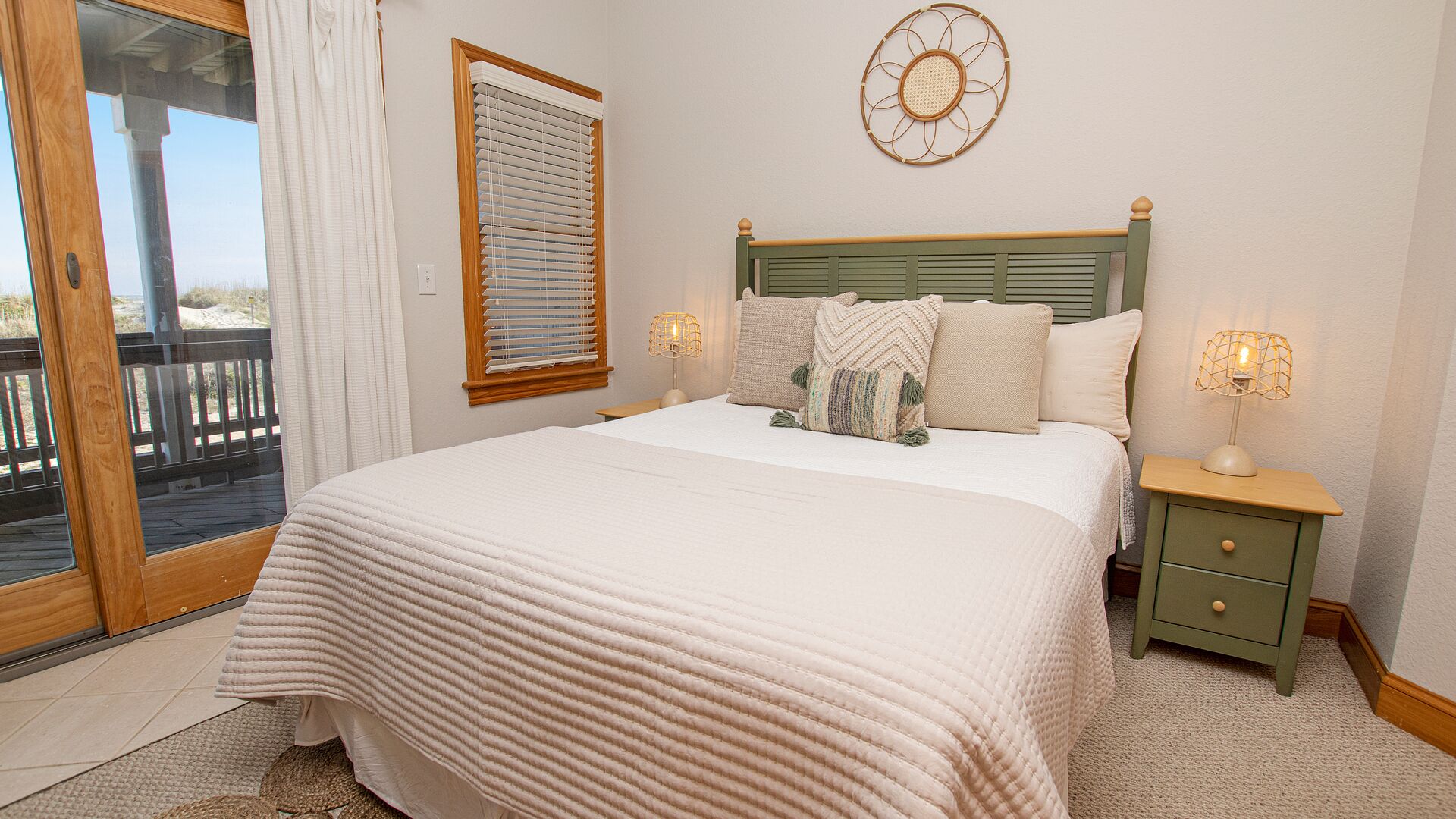 A bedroom with a large bed, two bedside tables with lamps, a window with blinds, and a decorative wall hanging.