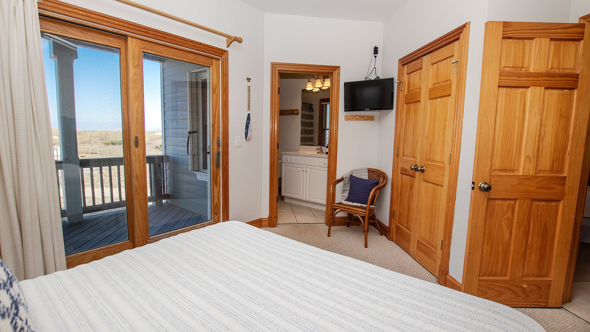 A bedroom with a large bed, wooden doors, a TV, and a view of the beach.