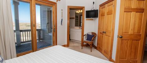 A bedroom with a large bed, wooden doors, a TV, and a view of the beach.
