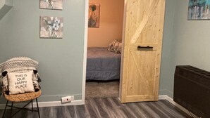Una habitación con una puerta corredera estilo granero, una silla con cojín y dos cuadros colgados en la pared.