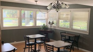 A dining area with four tables and chairs, large windows with blinds, and a chandelier. - Nature Coast Inn and Cottages (Inglis)