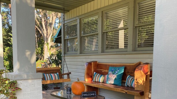 A covered porch with a wooden bench, a glass table with a 'WELCOME' sign, and potted plants. - Nature Coast Inn and Cottages (Inglis)