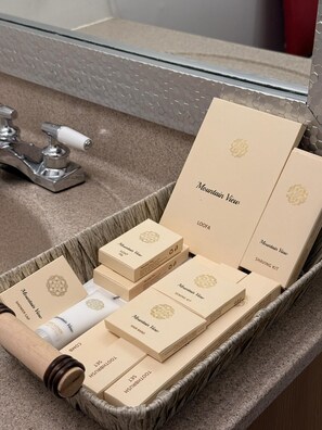 A bathroom with a sink, mirror, and a wicker basket containing toiletries and a shaving kit. - Mountain View Hope Motel (Hope)