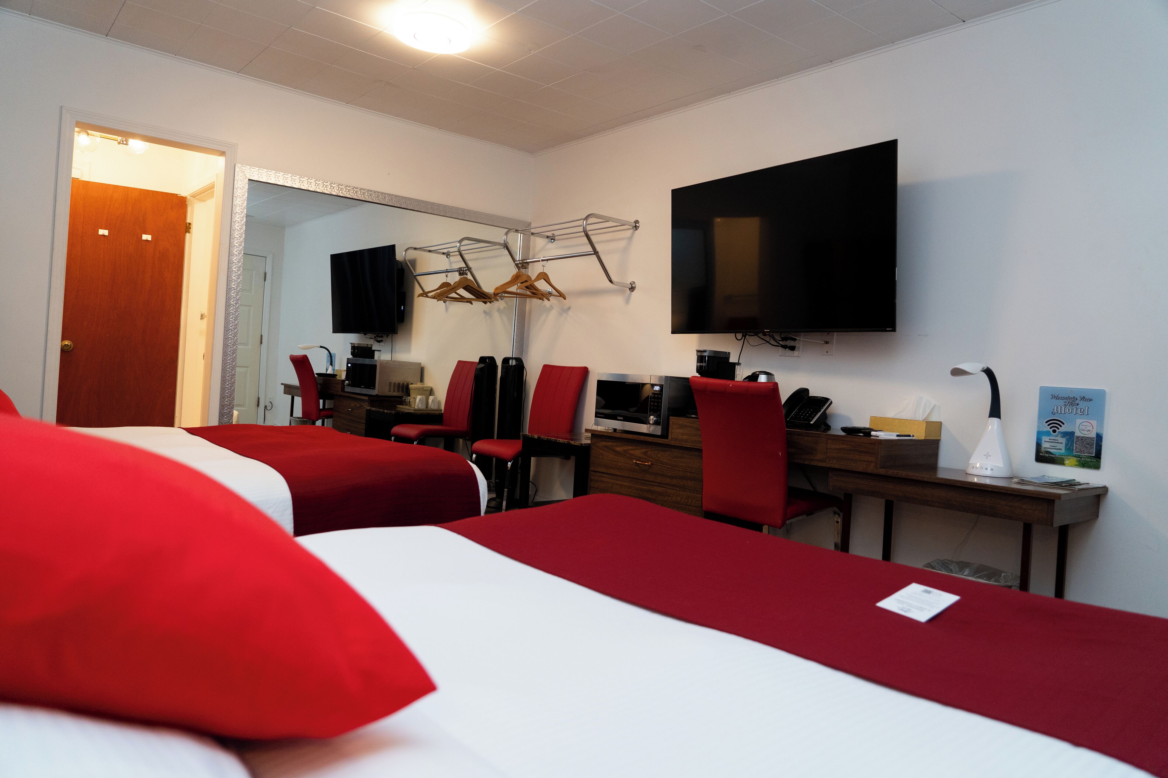 A hotel room with two beds, a desk with a computer, a flat-screen TV, and a mirror.