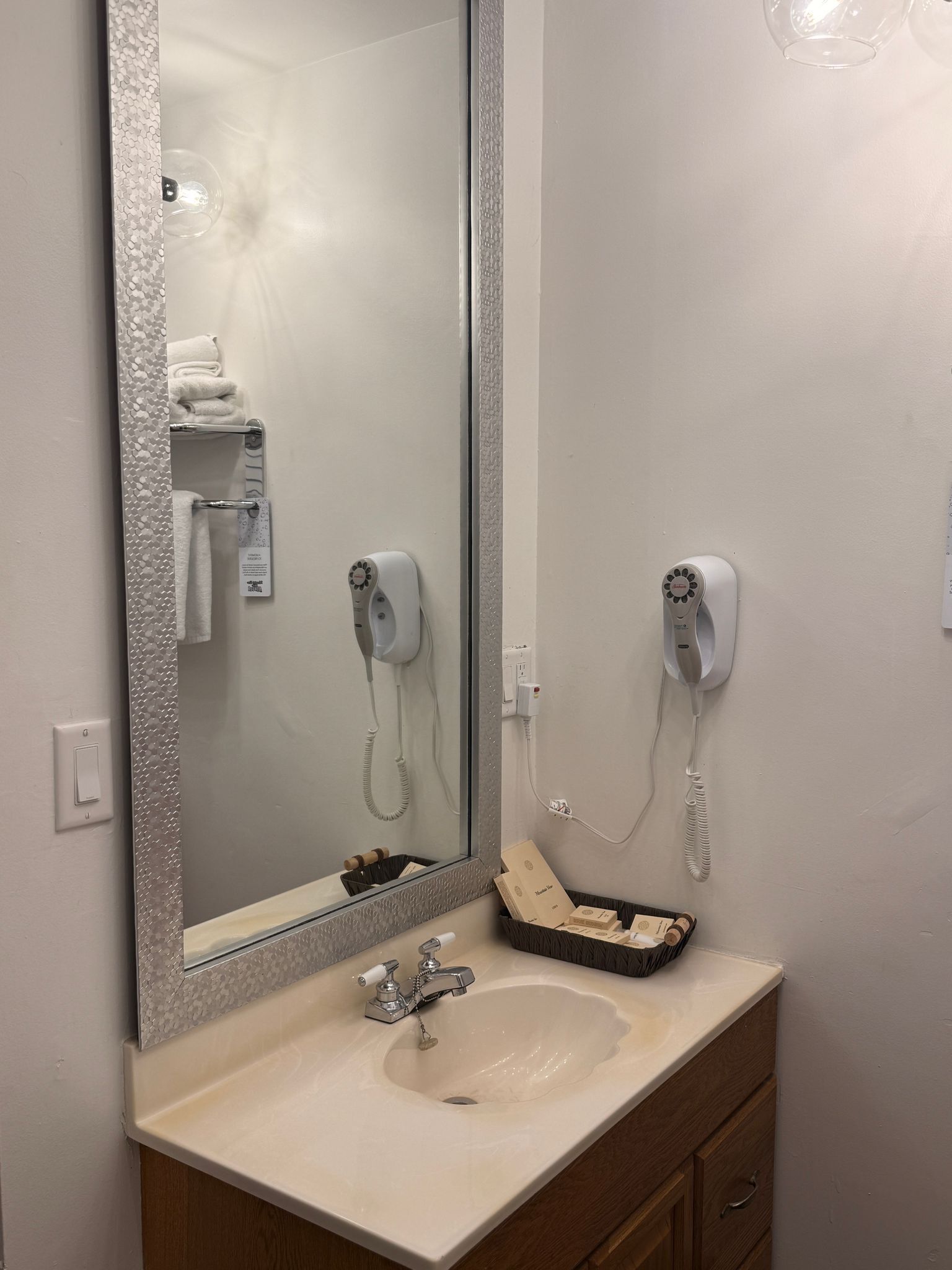 A bathroom with a large mirror, a sink, and two hair dryers mounted on the wall.