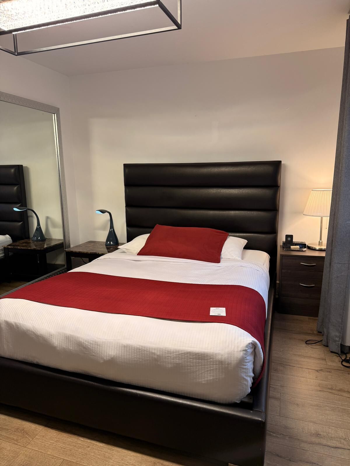 A hotel room with a large bed, a nightstand, a lamp, and a mirror.