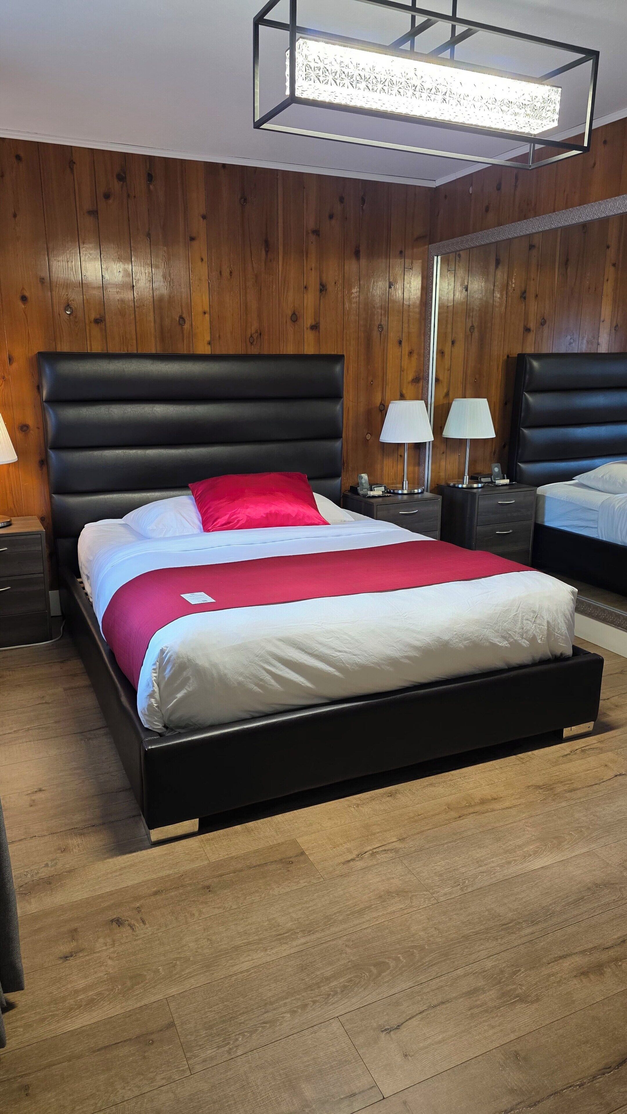 A modern bedroom with a large bed, two bedside tables, a nightstand, and a wooden wall paneling.