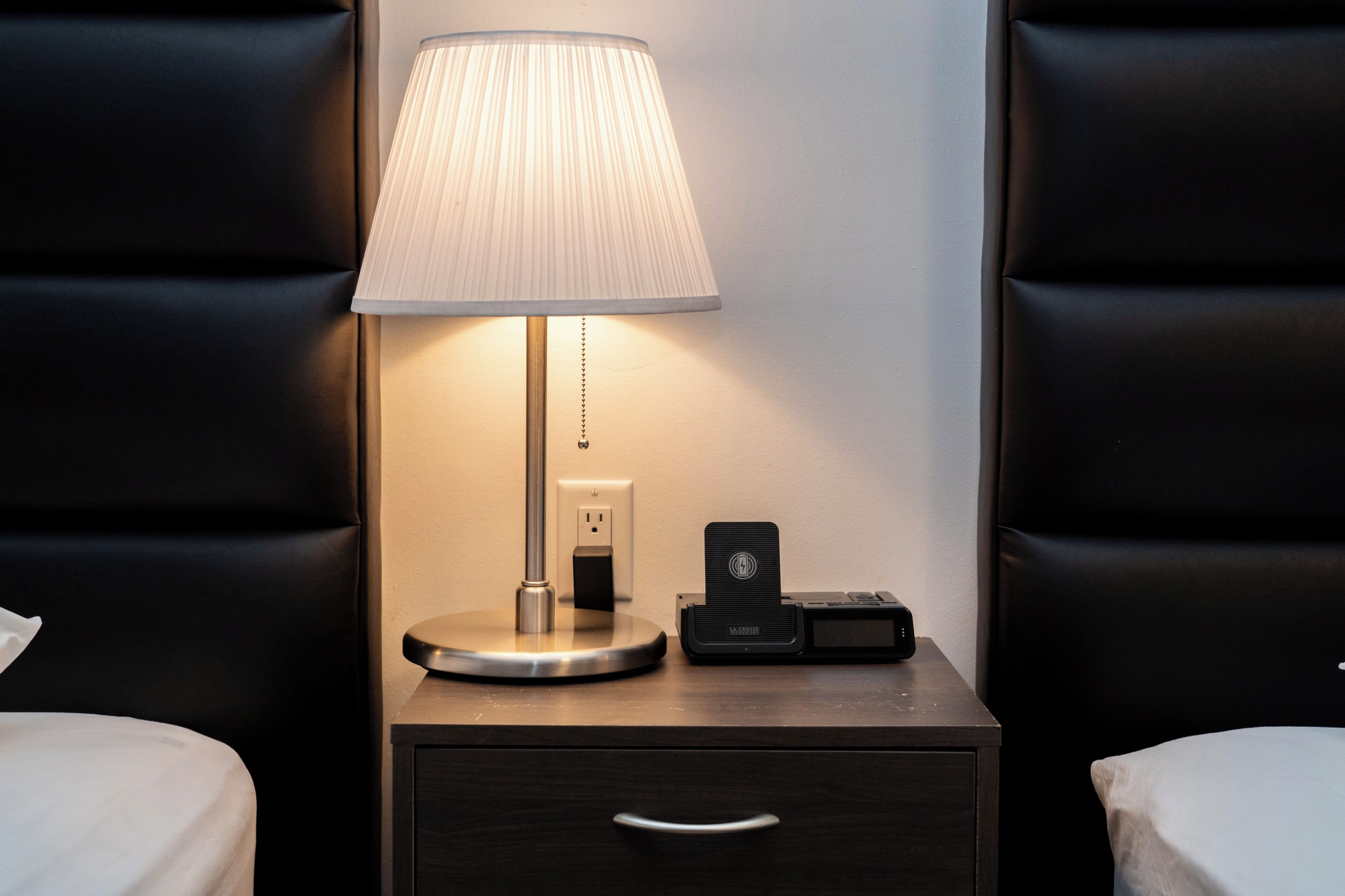 Une chambre d’hôtel bien aménagée, avec une table de chevet équipée d’une lampe, d’une prise de courant et d’une station de recharge.