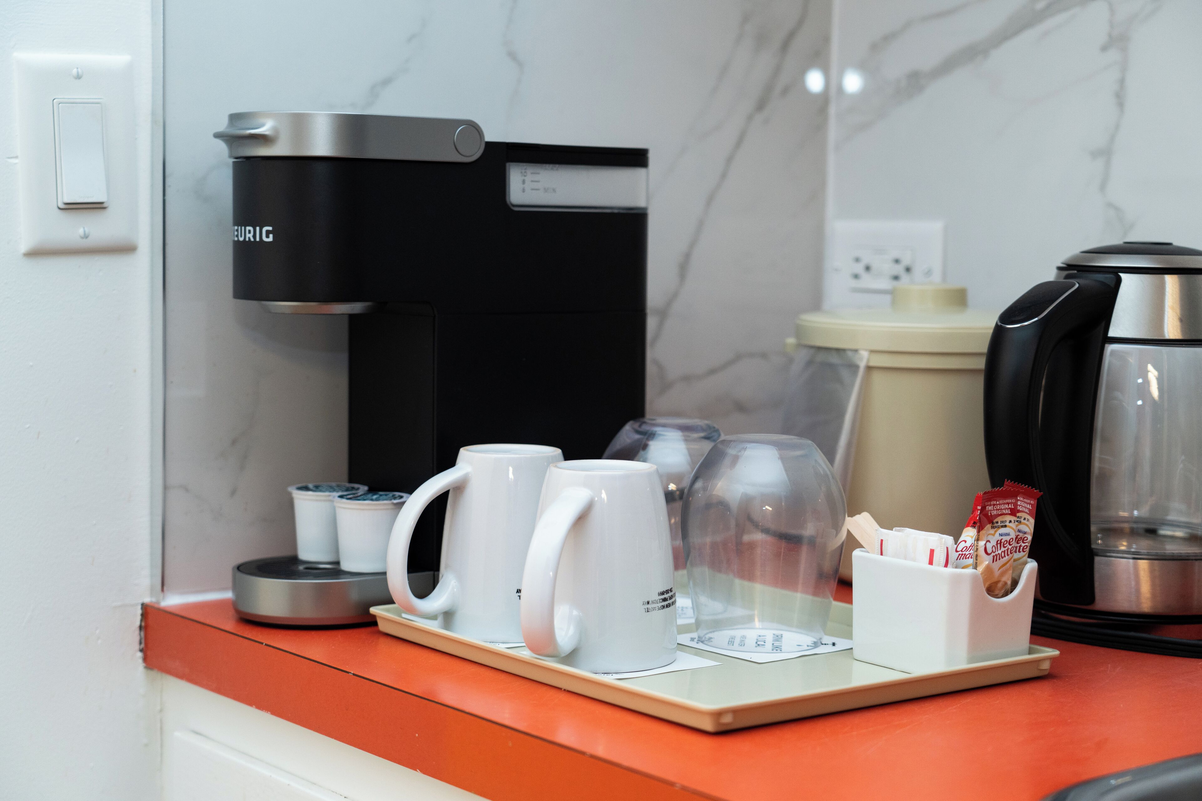 A coffee station with a Keurig coffee maker, two white mugs, a glass carafe, and a coffee pod holder.