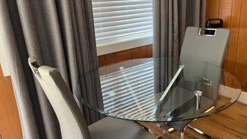 A modern room with a glass table and chairs, a window with blinds, and a wooden floor.