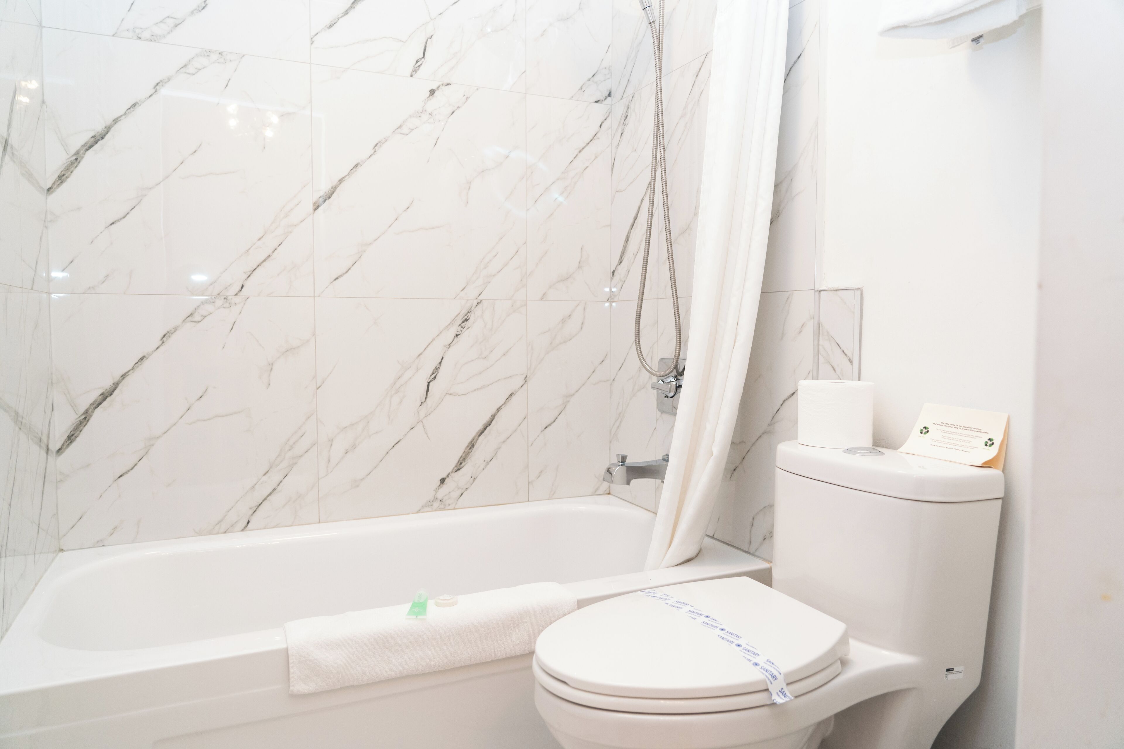 A bathroom with a bathtub, toilet, and marble walls.