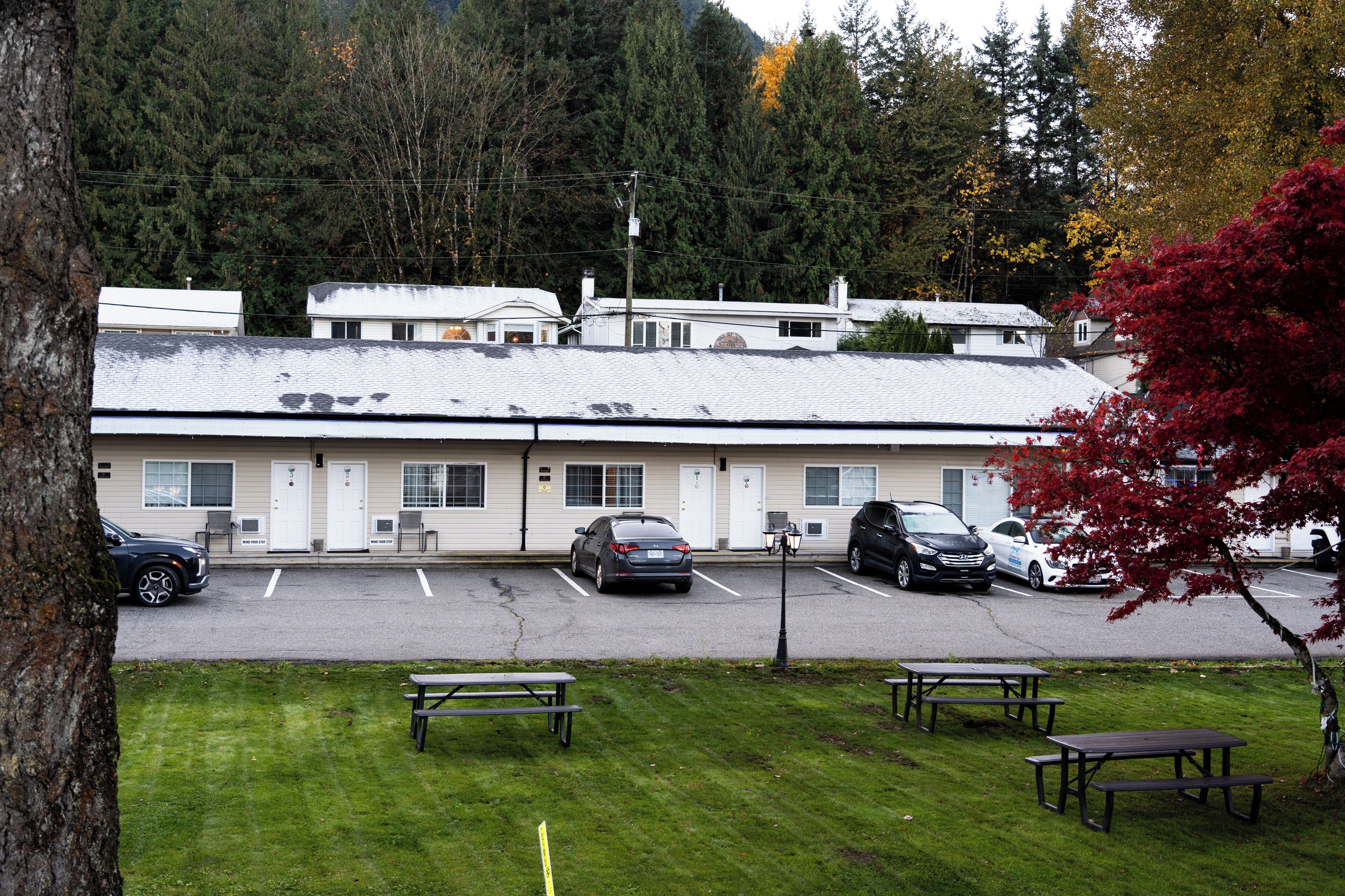 A motel with a parking lot, picnic tables, and a forested backdrop.