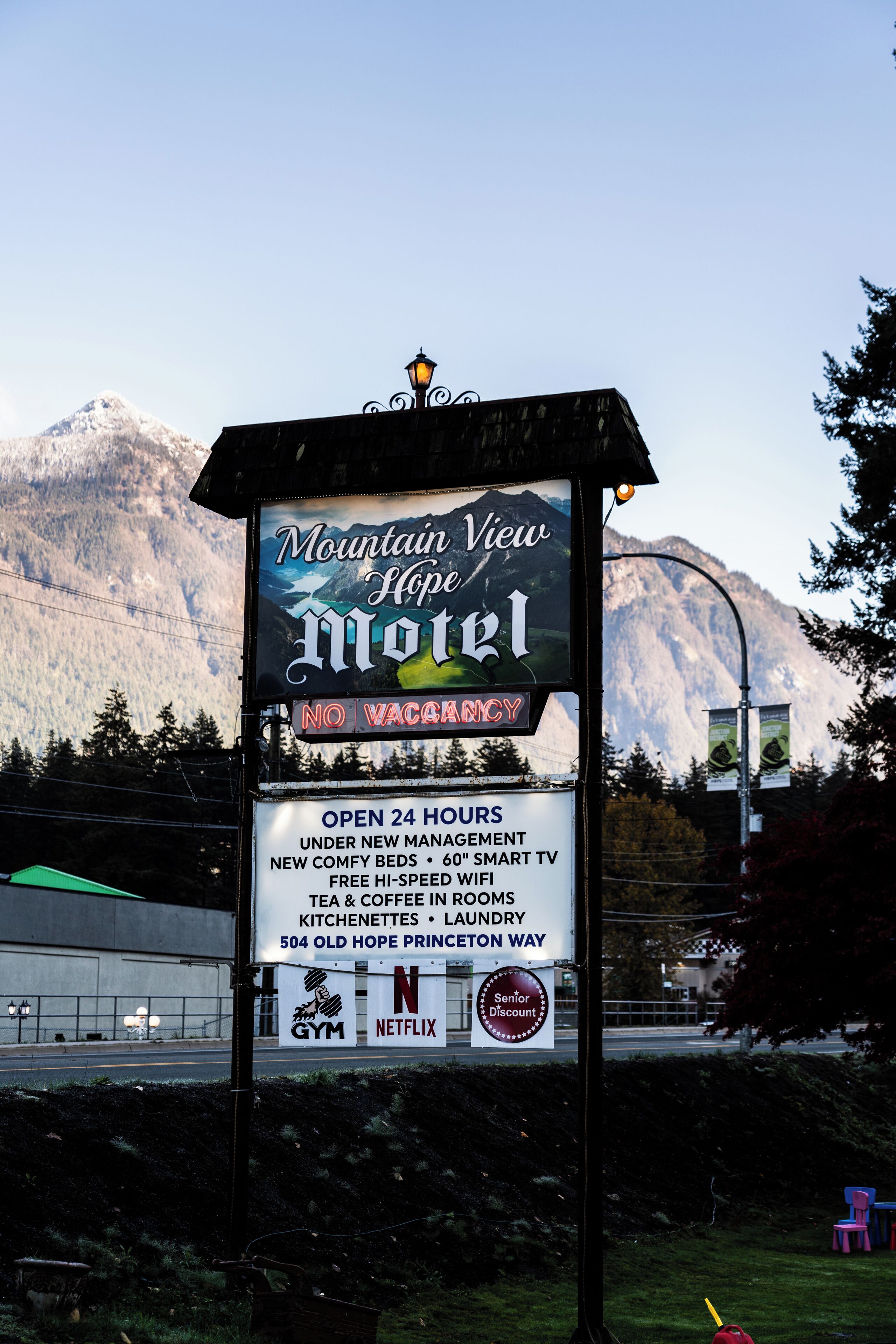A motel sign with amenities including 24-hour open hours, new comfy beds, smart TV, free high-speed WiFi, tea & coffee rooms, kitchenettes, and laundry.