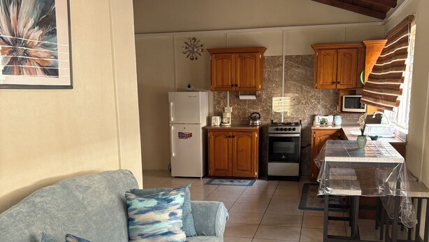 A living room with a sofa, a dining table, kitchen area with wooden cabinets, a refrigerator, and a stove.